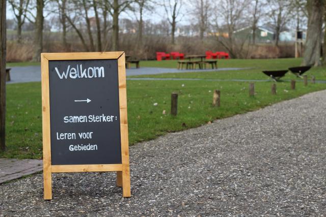 Grasveld met een krijtbord. Op het bord staat "Samen Sterker: Leren voor gebieden".